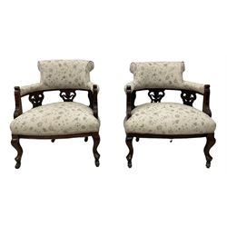 Pair late Victorian mahogany framed tub armchairs, scrolled back over pierced and carved foliate splats, sprung seat upholstered in ivory ground floral fabric, on cabriole supports with castors