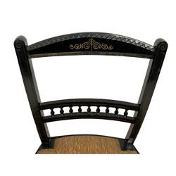 Late Victorian black lacquered low chair, the cresting rail with scrolling decoration, middle rail with turned spindle balustrade, rush seat on turned front supports joined by stretchers