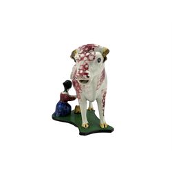 19th century cow creamer, probably Staffordshire, with curled tail handle, a milkmaid seated to one side with pail, decorated with sponged puce and set on concave green and black painted base, L20cm x H14cm