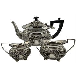 Late Victorian silver three piece tea set embossed with panels of flower heads and scrolls on ball feet, the teapot with ebonised handle and lift Birmingham 1898 Maker Joseph Gloster