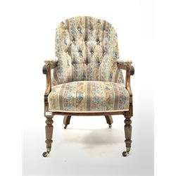 Late Victorian walnut framed open armchair, upholstered in buttoned fabric, floral scroll carved arm terminals, raised on turned supports with brass cup and ceramic castors, 