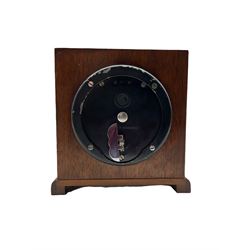 A compact mid-20th century English mantle clock in a square walnut case on raised feet, square brass dial with spandrels and silvered chapter ring, Roman numerals, five-minute Arabic’s, with a minute track and inner quarter hour track, steel serpentine hands within a square brass bezel and bevelled glass, spring driven movement by Elliot, London, with a balance wheel escapement and integral winding key.



