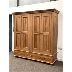 Solid pine four door wardrobe enclosing interior fitted for hanging, with three base drawers, raised on bun supports 