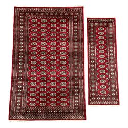 Persian Tekke Bokhara red ground rug, the field decorated with four rows of repeating Gul motifs, multi-band border with geometric design (244cm x 153cm); and a similar runner (188cm x 64cm)