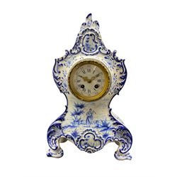 French Faience porcelain mantle clock with blue and white decoration c1890, in a rococo style case with scrollwork and floral decoration, the centre painted with a rural scene of a lady in 18th century costume, with a Parisian eight day rack striking movement stamped “Marti”, “medaille d' argent”, enamel dial with blue roman numerals, five minute Arabic's and minute track, gilt Louis XV style hands within a decorative cast bezel and plain slip with a flat bevelled glass, movement striking the hours and half-hours on a gong. With pendulum