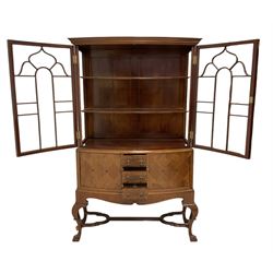 Early 20th century inlaid walnut bow-front display cabinet, dentil frieze over two astragal glazed doors enclosing two shelves, surrounded by chequered stringing, the base fitted with three central crossbanded drawers, flanked by two marquetry cupboards, shaped apron over cabriole supports, united by moulded shaped X-stretcher