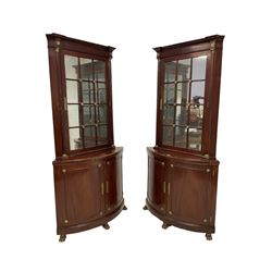 Pair of French Empire design corner cabinets, the straight-front upper section with canted corners and applied half-column pilasters, enclosed by mirror glazed door, the bow-front lower section enclosed by two doors with applied mouldings, mounted by cast metal floral rosettes, skirted base with cast gilt metal hairy paw brass feet
