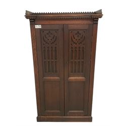 Victorian oak freestanding cupboard, lappet carved cornice over two blind-fretwork doors of gothic design, enclosing three shelves, skirted base