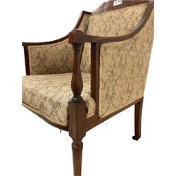 Edwardian inlaid mahogany upholstered armchair, cresting rail with scrolling foliate satinwood inlays and ebony stringing, upholstering in floral patterned fabric with sprung seat, on tapering supports and castors