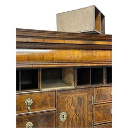 George I walnut cabinet on chest, the projecting stepped and moulded cornice over single cushion drawer, the two feather banded cabinet doors opening to reveal a fitted interior comprising of four pigeonholes concealing secret drawers, eleven assorted drawers with a central cupboard, the figured walnut facias with feather banding and drop pull handles in the form of masks, the lower section fitted with three graduating drawers with moulded facias and press brass plates and escutcheons, raised on shaped bracket feet