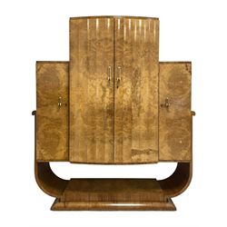 Attributed to Harry & Lou Epstein - Art Deco circa. 1930s figured walnut cocktail cabinet, enclosed by two scallop fluted doors, the maple and mirrored interior fitted with shelves, slide and cupboard, flanked by two side cupboard with internal drawers, curved supports on undertier with moulded base