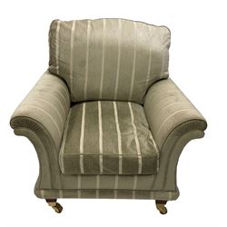Traditional shaped armchair with scrolled arms, upholstered in pale sage striped fabric, raised on tapered supports with brass cups and castors