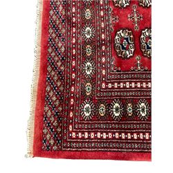 Persian Tekke Bokhara crimson ground rug, the field decorated with three rows of repeating Gul motifs, the multi-band border with stylised plant motifs in contrasting colours and geometric designs
