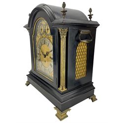 Edwardian - English ebonised 8-day bracket clock in a break arch case with flambe finials and reeded columns with Corinthian capitals to the front, silk backed brass side frets on an ogee plinth raised on bracket feet, brass dial with matted centre, slivered chapter ring and conforming dials for chime selection and chime/silent, three train chain driven fusee movement with an engraved backplate sounding the quarters on 8-bells and the hours on a coiled gong.  With pendulum and key.
