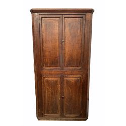 Early 19th century floor standing country oak corner cupboard, with four fielded panelled doors enclosing three shelves, raised on skirted base W110cm