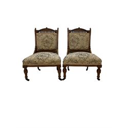 Pair of Victorian bedroom chairs, the carved cresting rail over back and seat upholstered in floral fabric, raised on turned supports, terminating in ceramic castors 