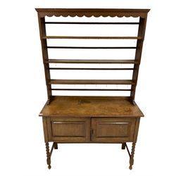 Early 20th century oak dresser and rack, rectangular top over scalloped frieze and three shelves with brass hooks, the base fitted with two panelled doors over knulled turned front supports 