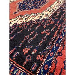 Persian senneh hand knotted red ground rug centred by a geometric medallion and bordered 165cm x 120cm
