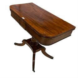 Early 19th century mahogany card table, rectangular fold-over and swivel top with rounded front corners, turned pedestal with plinth base and four splayed sabre supports with carved reeding, on brass castors