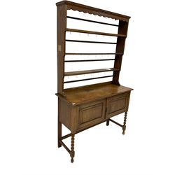 Early 20th century oak dresser and rack, rectangular top over scalloped frieze and three shelves with brass hooks, the base fitted with two panelled doors over knulled turned front supports 