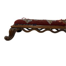 Victorian mahogany hearth stool, seat upholstered in foliate patterned tapestry beadwork, applied curved frieze, raised on scrolled cabriole feet (W135cm); 19th century walnut ecclesiastical kneeler stool, upholstered in floral needlework, the figured base with applied gilt cross mounts(W108cm)