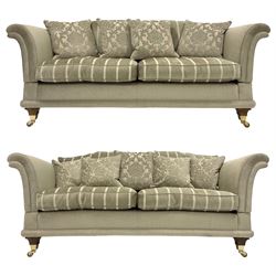 Large pair traditional design drop-arm two seat sofas, shaped back and scrolled arms, upholstered in textured pale sage fabric with striped seat cushions, raised on tapered feet with brass cups and castors