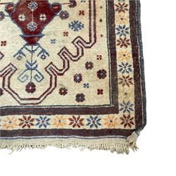 Persian Baluchi ivory ground rug, the field with a shaped crimson outline encasing a stylised urn and plant motif with geometric qualities, the triple band border with repeating star motifs in indigo and red