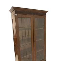 20th century oak bookcase, the projecting cornice and carved frieze over two leaded glazed doors opening to reveal three adjustable shelves, over cupboard, raised on a plinth base W90cm, H190cm, D37cm