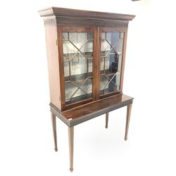 Early 20th century Chippendale style mahogany bookcase on stand, dentil cornice over carved frieze and two astragal glazed doors enclosing two shelves, the bottom section with matching carved frieze and raised on square tapered supports with peg feet W107cm, H182cm, D51cm