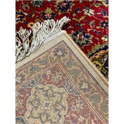 Persian design red ground carpet, the central floral medallion surrounded by stylised plant motifs and lanterns, the field decorated by interlacing foliate decoration, the guarded border decorated with repeating shaped floral panels 