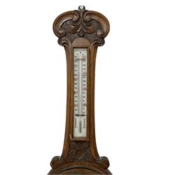 Mid-20th century mercury stick barometer and an early 20th century aneroid wheel barometer. Mahogany stick barometer with a broken pediment and brass finial, silvered register with engraved predictions and vernier, unenclosed bulb cistern tube with mercury present. Carved oak aneroid barometer with an 8” porcelain dial, predictions, and a boxed mercury thermometer above, steel indicating and recording hands within a brass bezel with a flat beveled glass.