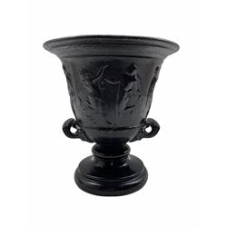 19th century black painted iron two handled pedestal vase, with a raised frieze of dancing and musical figures on a ceramic foot H27cm