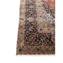 Persian Kashan carpet, red ground field with blue central medallion and spandrels, all-over floral design with stylised plant motifs and interlacing foliate, guarded border with scrolling designed decorated with floral motifs