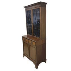 Early 20th century inlaid mahogany bookcase on cabinet, projecting dentil cornice over two astragal glazed doors enclosing adjustable shelves, crossbanded and ebony-strung top, fitted with two drawers over two panelled cupboard doors, on bracket feet