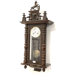 Late Victorian walnut and oak Vienna style wall clock, the case surmounted by a carved prancing horse and mask pediment over turned pilasters and glazed door, white enamel dial with Roman chapter ring, eight day movement striking hammer on coil 